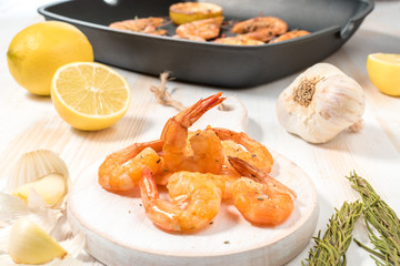 Grilled shrimps with lemon, paprika, spices and herbs on a white wooden board.