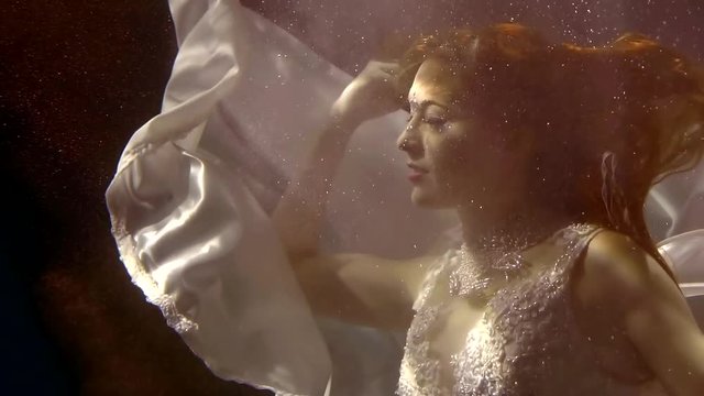 a woman who looks like a fairy-tale character swims under the water, light hits her