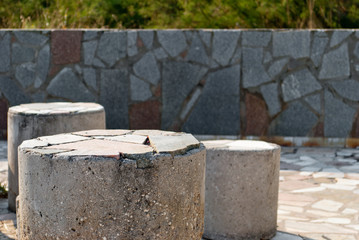 Composition of three low concrete stone pillars, against a background of a large stone tile texture, mosaic, bright summer sunny day, fence stone fence