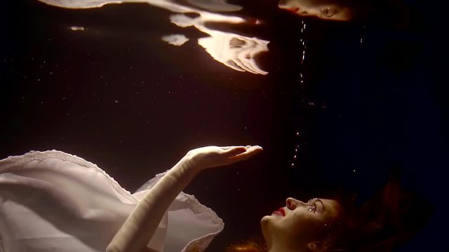 a young woman who swims under the water in a white dress touches her reflection, a mystical tale