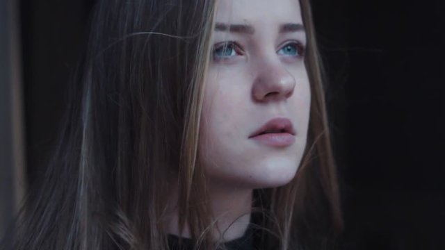 attractive lonely blue-eyed confused troubled girl looking around, while wind blowing in her face on the dark background. Wind playing with hair. Natural beauty, negative feelings