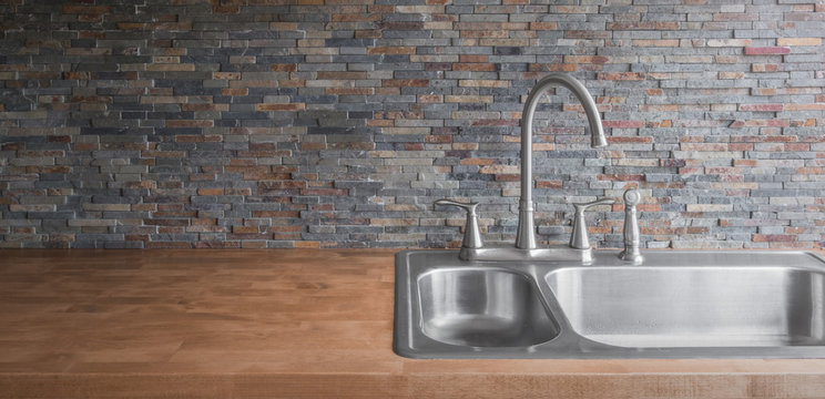 Wooden countertop with a modern stainless steel sink and faucet and a stone tile backsplash
