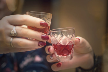 People is clinking glasses with alcohol drinks and says a toasts. Close up photo of hands with glass with alcohol. Festive table.