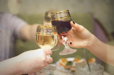 People is clinking glasses with alcohol drinks and says a toasts. Close up photo of hands with glass with alcohol. Festive table.