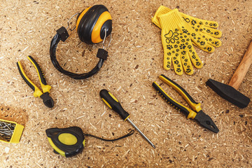 Top view of working tool: noise insulated headphones, tape measure, yellow gloves, wrench, screwdrivers, hammer, pliers, nippers close-up on wooden texture table. Flat lay copy space for advertisement