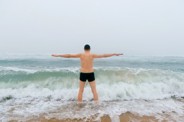 Fototapeta premium Odd bizarre crazy fearless awesome adult man enjoying in cold stormy sea. Guy jumping in waves in ocean with emotional funny face. Adult male fooling like child in water outdoors. Leisure activities