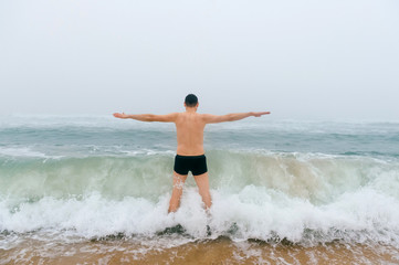 Fototapeta premium Odd bizarre crazy fearless awesome adult man enjoying in cold stormy sea. Guy jumping in waves in ocean with emotional funny face. Adult male fooling like child in water outdoors. Leisure activities