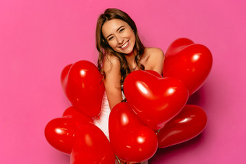Happy Valentine's day. Attractive shy woman, widely smiling, posing at camera with heart-shaped balloons.