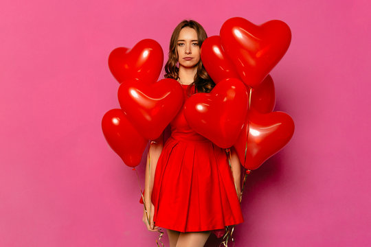 Attractive Woman With Frustrated Face, Holds Heart Shaped Air Balloons. St. Valentine's Day.