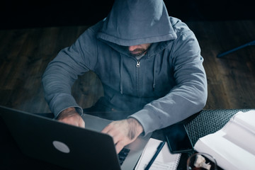 guy hacker in a sweatshirt with a hood sits behind a laptop
