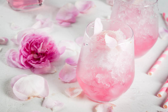 Summer refreshing desserts. Vegan diet food. Ice cream frozen rose, froze, with rose petals and rose wine. On a white concrete table, with spoons, striped straws, petals and rose flowers. Copy space
