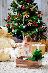 A beautiful little baby is playing around a Christmas tree