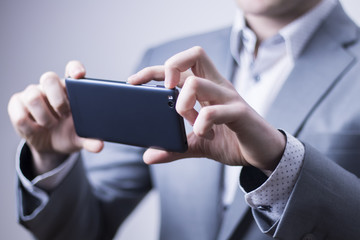 Closeup of a businessman in grey suit taking picture with a mobile phone