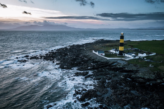 Aerial of the atlantic coast and black and blue lighthouse in Ireland near the ocean and sunset