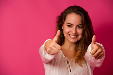 Beautiful young woman showing thumb up as a gesture for success isolated ovwe pink background