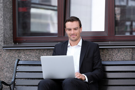 Man sitting on bench outdoors and using laptop