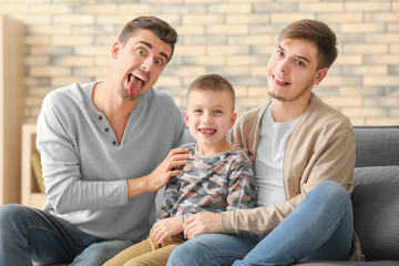 Funny male gay couple with adopted boy on sofa at home