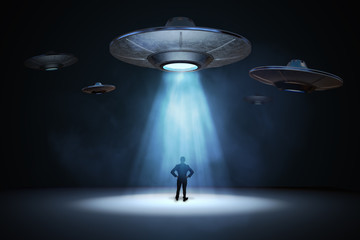 Alien invasion concept. Man standing under light beam from flying UFO spaceship. 3D rendered illustration. © vchalup