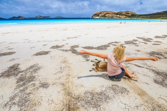 Happy caucasian woman with open arms near a Kangaroo lying at Lucky Bay in Cape The Grand National Park, Esperance, Western Australia. Female tourist enjoys one of the WA's most famous beaches.