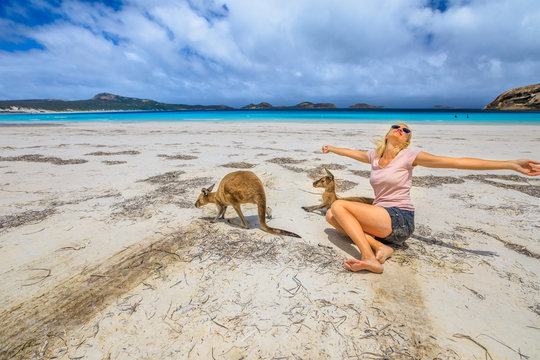 Happy caucasian woman with open arms near a two Kangaroos at Lucky Bay in Cape The Grand National Park, Esperance, Western Australia. Female tourist enjoys one of the WA's most famous beaches.