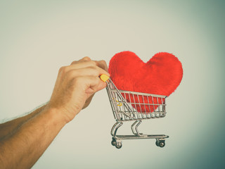 Male hands holding shopping cart with heart.