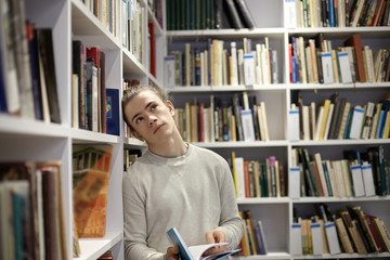 Cropped shot of romantic 20 year old young European man standing in bookstore with open book in his hands, looking up, having thoughtful dreamy look, reading good poem. People, leisure and hobby