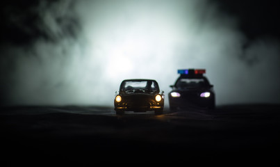 Obraz na płótnie Canvas Toy BMW Police car chasing a Ford Thunderbird car at night with fog background. Toy decoration scene on table . Selective focus – 11 JAN 2018, BAKU AZERBAIJAN