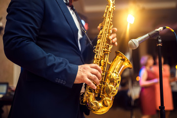 young musician man plays tenor saxophone on stage with light bokeh effected over blurred music instrument background
