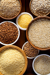 Various groats, cereals. Different types of groats in bowls on a wooden background, top view, close up. Healthy nutrition food