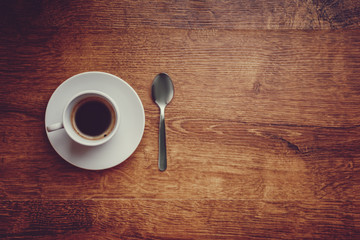 top view of white Cup with black coffee on a white saucer and teaspoon on dark brown wooden background