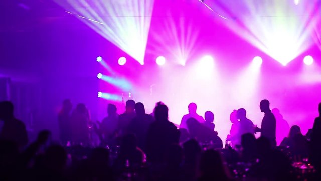 A youth party in a restaurant or a nightclub, banquet tables with alcohol and food against the background of silhouettes of dancing people, stage light and purple fill