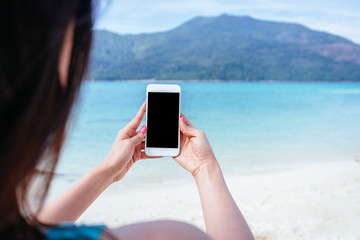 Woman holding blank screen smartphone mobile with beautiful sea and island in background