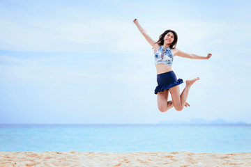 Happy and cheerful young Asian woman jumping on the beach in morning