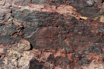 A close-up of a surface of treated rose granite rock plate. A fragment of a stone wall decoration. Texture of deep rose granite facing material.