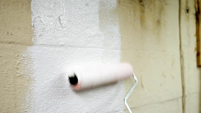 Using a roller to apply a waterproofer sealant onto unfinished basement wall