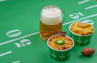 closeup of chili and mug of beer and football decorations on table for game day