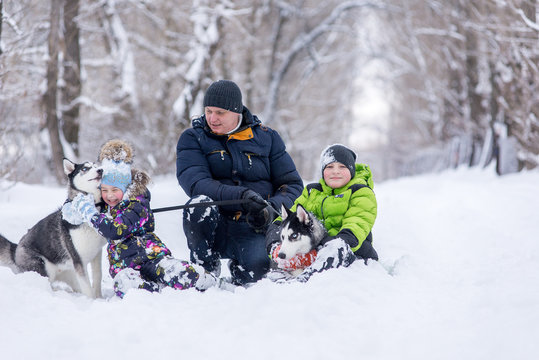 father with his son and daughter, and with two dogs the husky playing in the snow in the park in the winter.