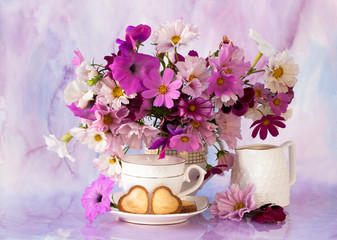 bouquet of chamomile and pepunium in a jug and a cup of tea with biscuits