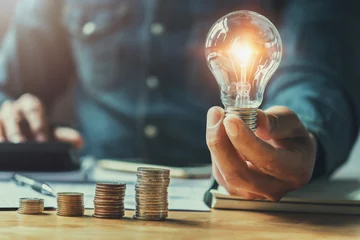 Fotobehang business man hand holding lightbulb with using calculator to calculate and money stack. idea saving energy and accounting finance in office concept © lovelyday12