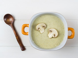Yellow bowl cream soup of mushrooms with croutons and wooden spoon on white table. The view from the top.