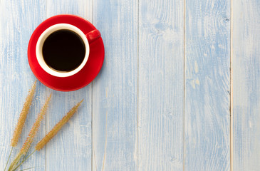 The grass flowers and red cup coffee on a wooden floor have a blue wooden floor as background.