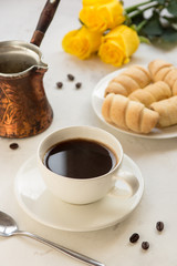Coffee, jezva and sweet bakery on a white table, yellow roses on a background