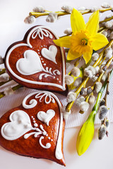 Traditional Czech easter decoration - homemade gingerbread hearts cakes with pussycats and daffodils flowers on white background. Spring easter holiday arrangement.