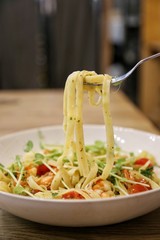 using stainless fork pick pasta / linguine with scrimp scampi in a white dish on a wooden table up