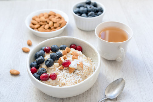 Oatmeal porridge bowl with almonds, blueberries, cranberries and coconut. Cup of green tea on side. Healthy eating, healthy lifestyle, healthy breakfast food concept