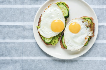 Toast with avocado, egg and cucumber on white plate. Table top view, copy space for text