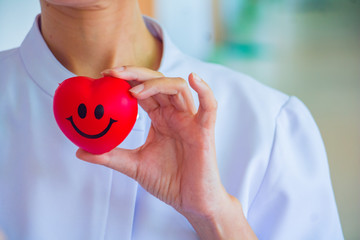 A nurse holding red heart toy. She is Left / right hand holding it.The photo shows the principle of caring and good health.