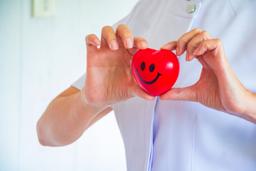 A nurse holding red heart toy. She is Left / right hand holding it.The photo shows the principle of caring and good health.
