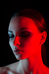 Studio portrait of girl with closed eyes and red ligth on a face closeup