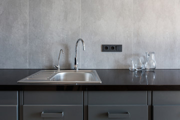 Detail of a rectangular designer kitchen sink with chrome water tap